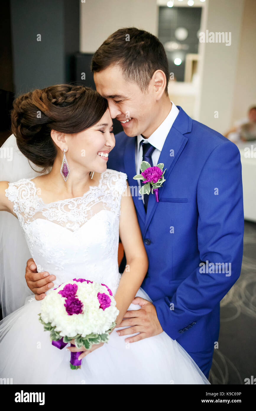 Charming couple bride and groom in the lobby laughing and genuinely smiling positive portrait. Sincere feelings, strong emotions. Wedding bouquet in hands, all in one color scheme. Stock Photo