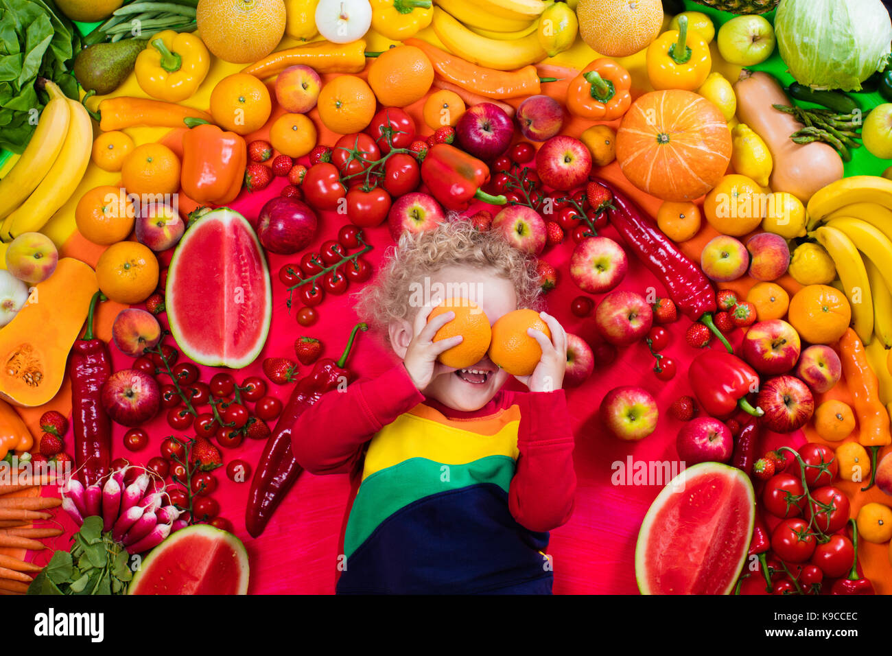 Baby boy with variety of fruit and vegetable. Colorful rainbow of raw fresh fruits and vegetables. Child eating healthy snack. Vegetarian nutrition fo Stock Photo