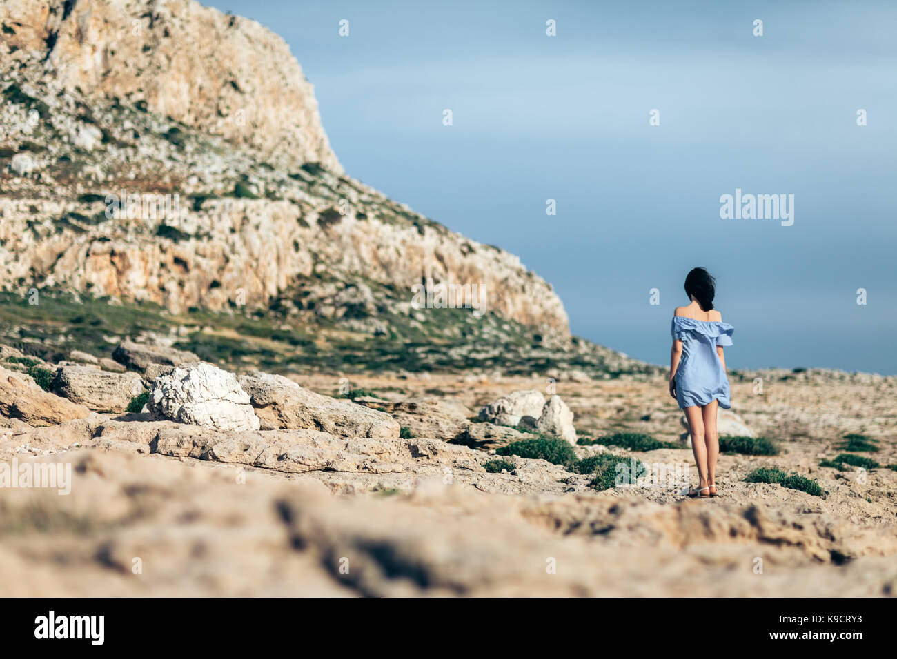 Back view of lonely woman walking on rocky desert with dramatic sky Stock Photo