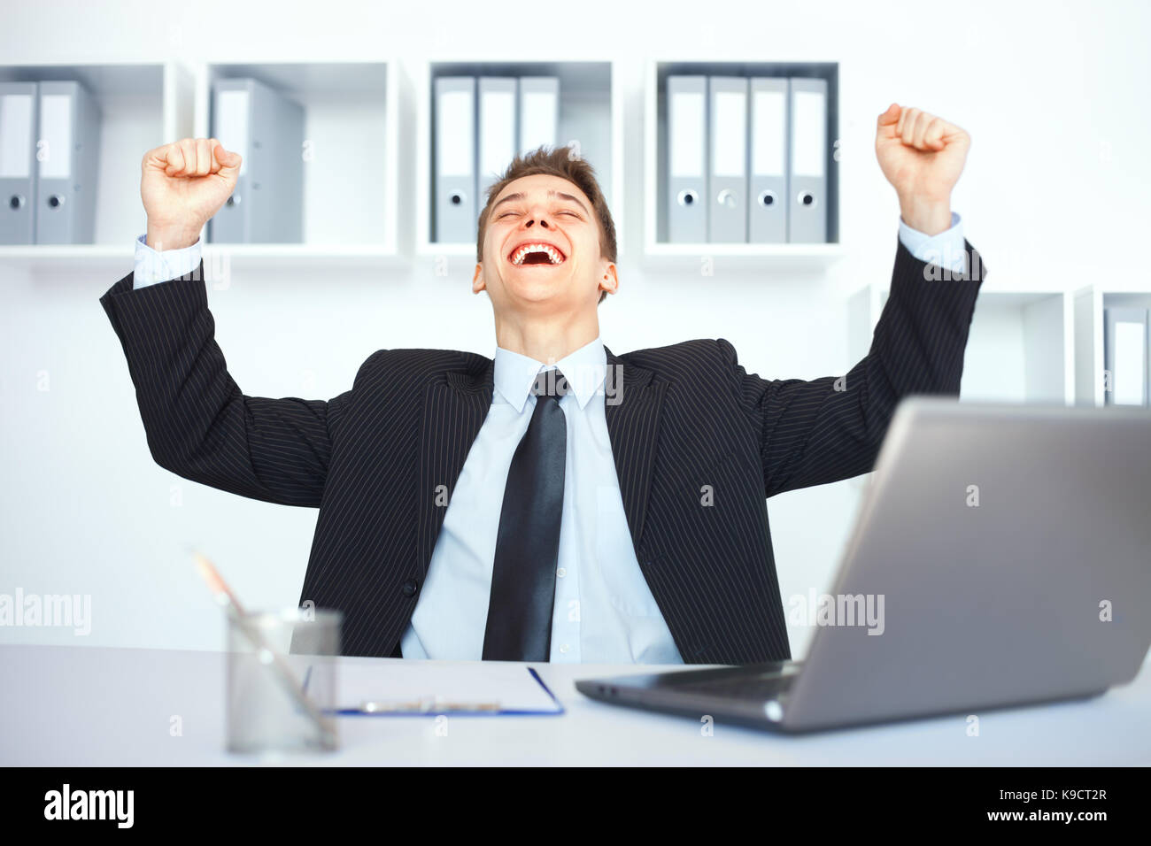 Young businessman celebrating his success with arms raised at his ...