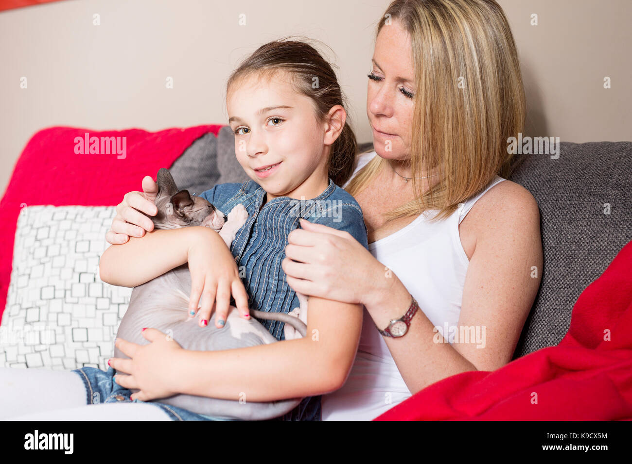 A Little girl with mother and cat on sofe at home Stock Photo