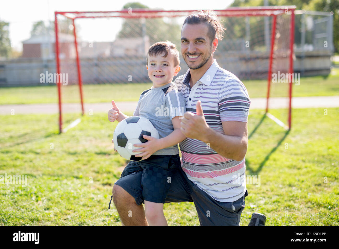 A man with child playing football outside on field Stock Photo