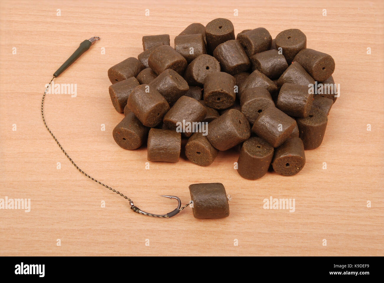 Fishing bait with hook and brown pre-drilled halibut pellets for carp  fishing isolated on wood background with soft shadow Stock Photo - Alamy