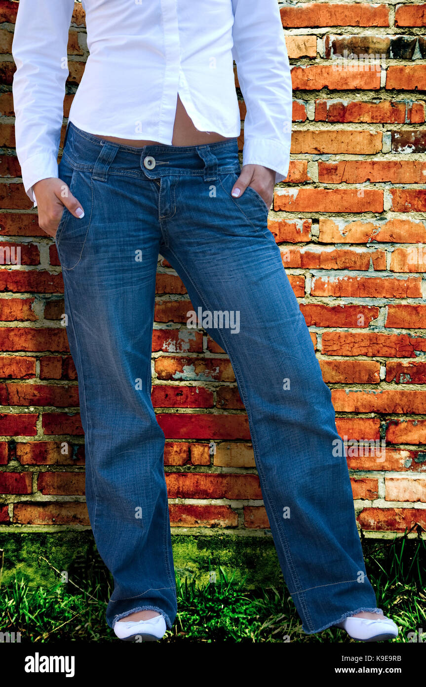 woman with white shirt and blue jeans, half body, no face seen, in front of a bricks wall Stock Photo