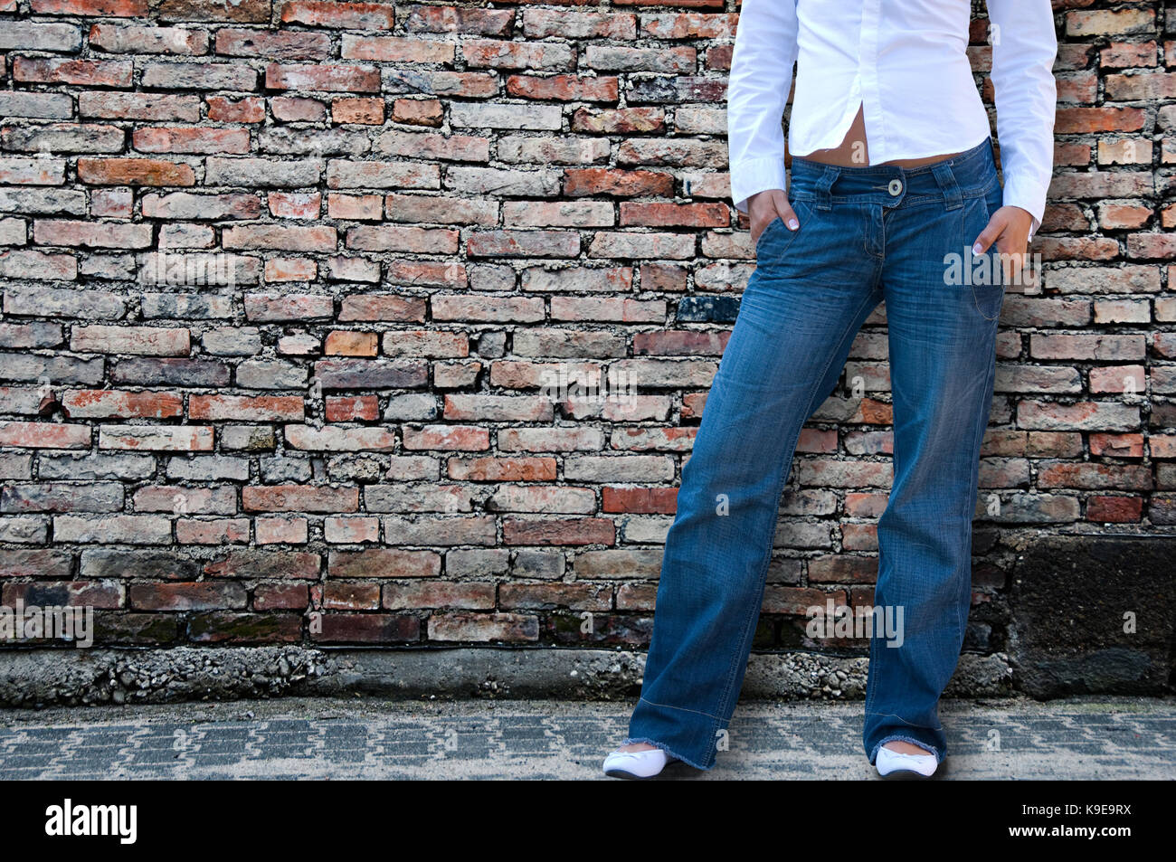 woman with white shirt and blue jeans, half body, no face seen, in front of a bricks wall Stock Photo