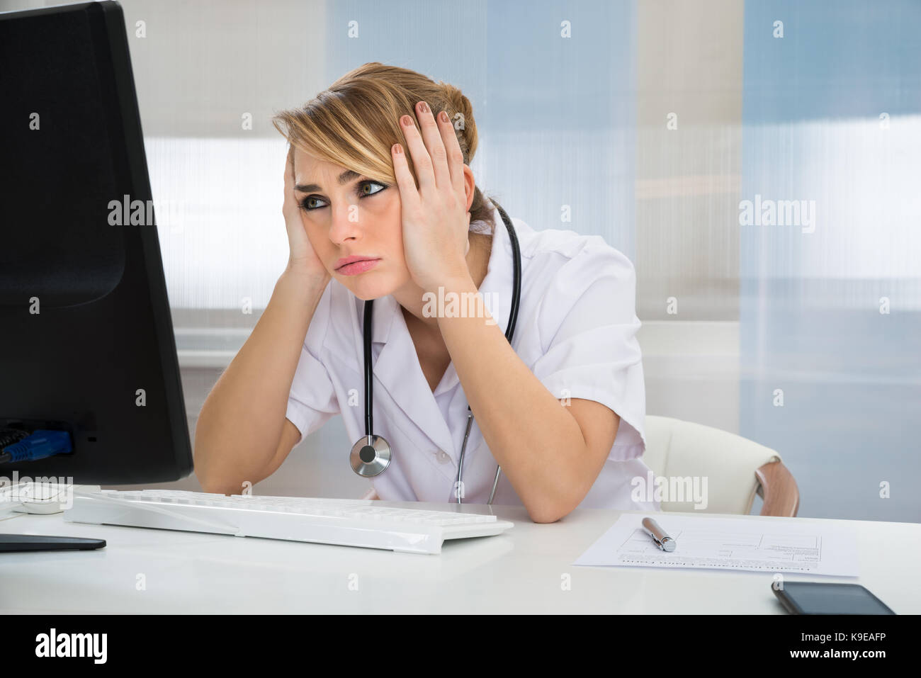Young Female Worried Doctor Looking At Computer In Clinic Stock Photo