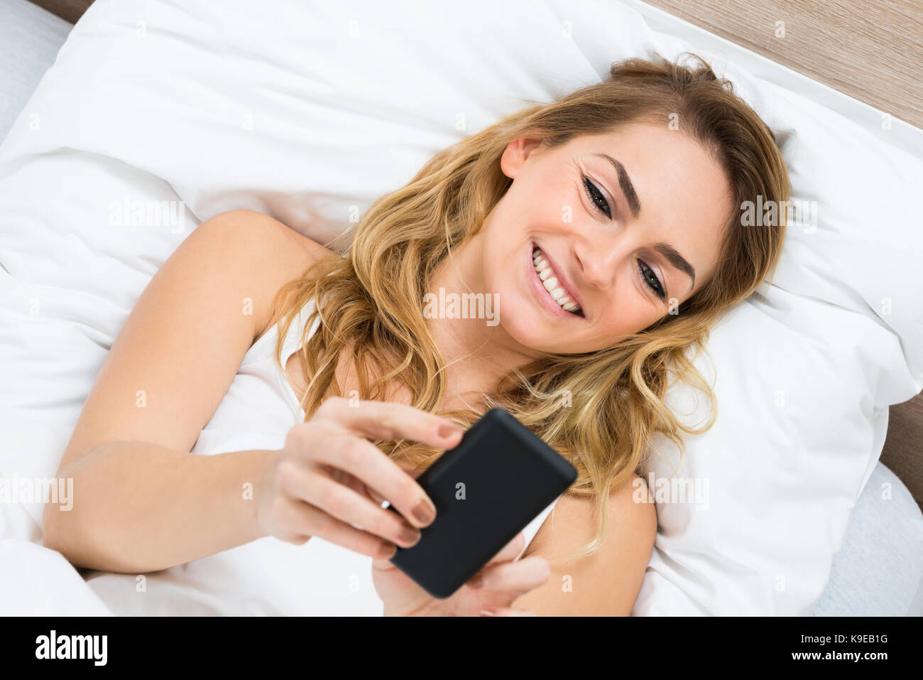 High Angle View Of A Woman Lying On Bed Using Cellphone Stock Photo