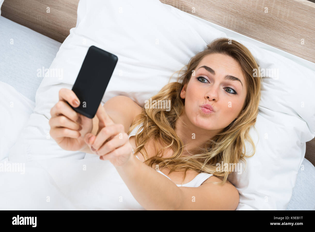 High Angle View Of A Young Woman Lying On Bed Taking Selfie Stock Photo