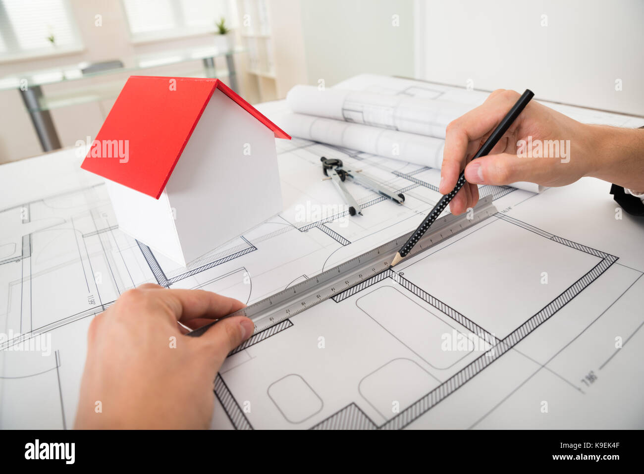 Close-up Of Engineer Drawing Diagrams In Front Of House Model On Blueprint Stock Photo