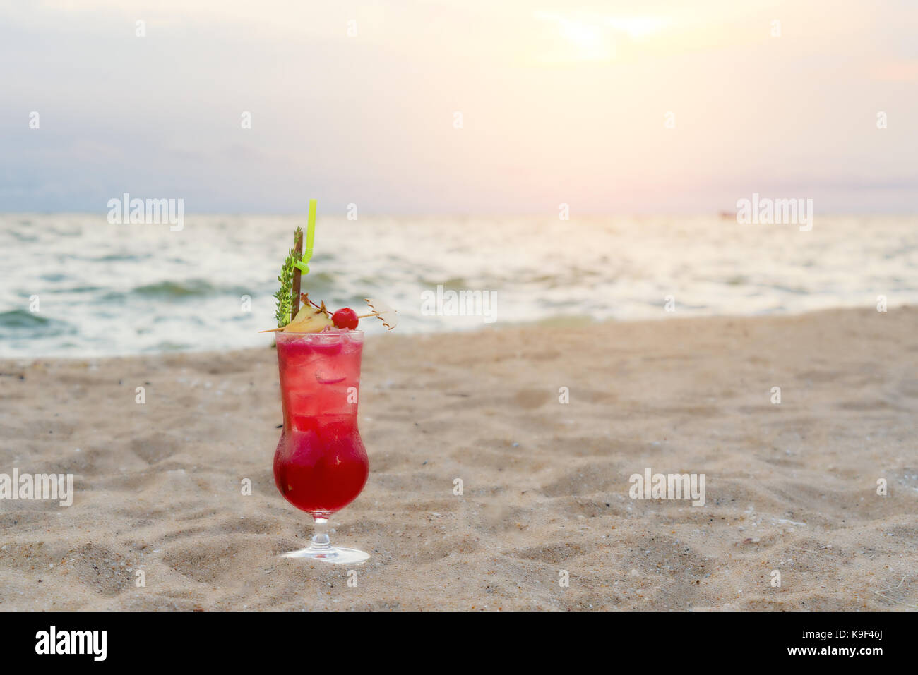 Red cocktail drink on sand in beach in twilight sea & sky background. Summer, Vacation, Travel and Holiday concept. Stock Photo