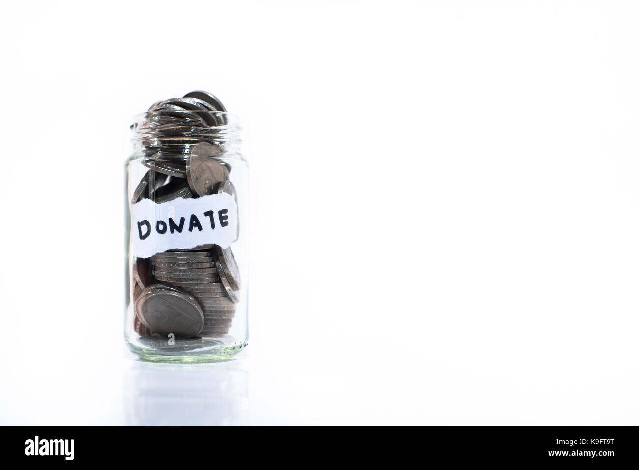 Coins in glass jar with a note written ' DONATE '. Isolated on a white background. Saving money to help others. Donation concept and Saving concept. M Stock Photo