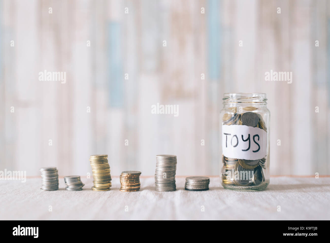 Stacked coins and coins in a glass jar with label written TOYS. Saving money to buy dream toys.Saving concept Stock Photo