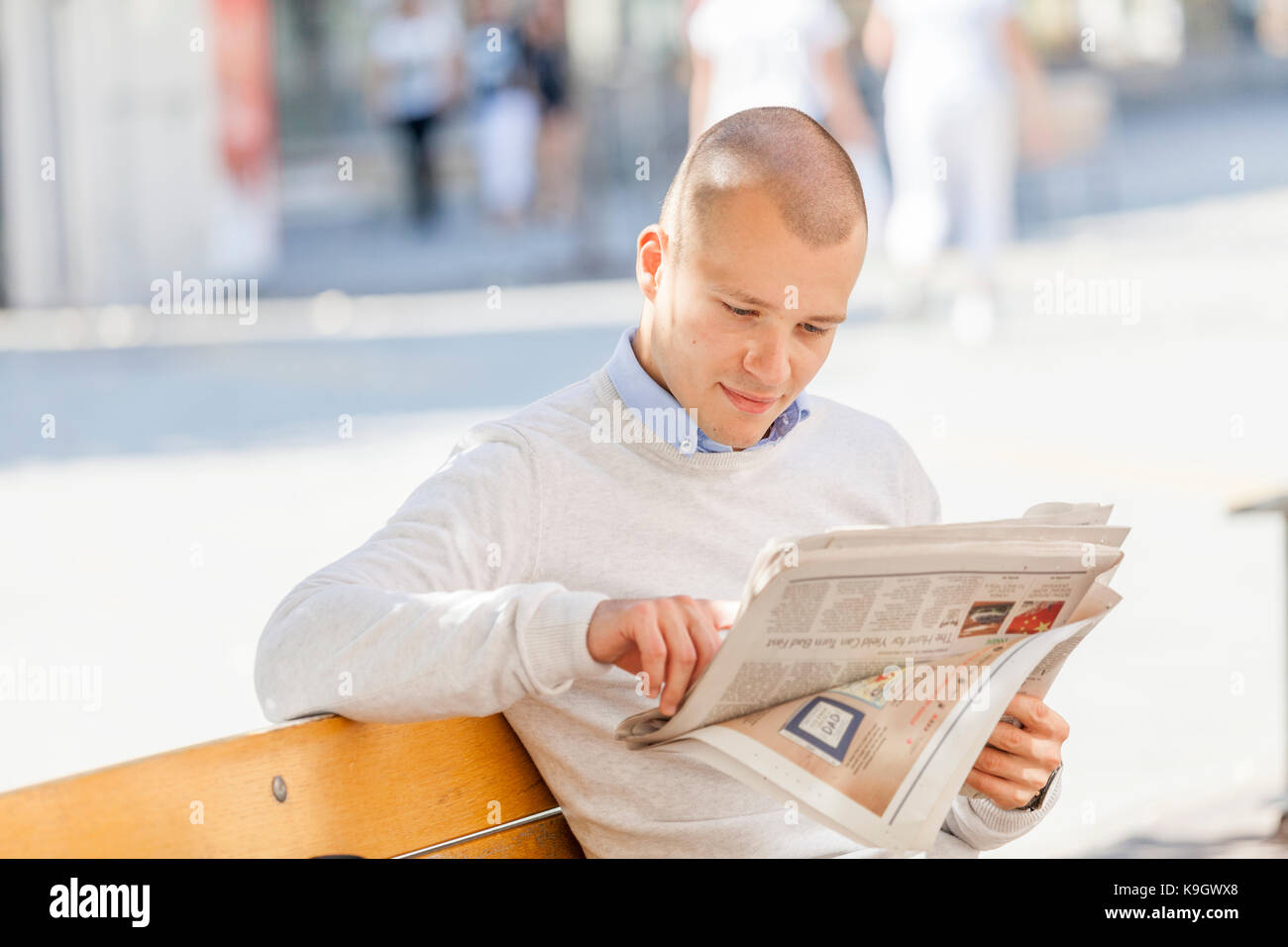 Young businessman sits at a table in the summer garden of a cafe and reads newspapers Stock Photo