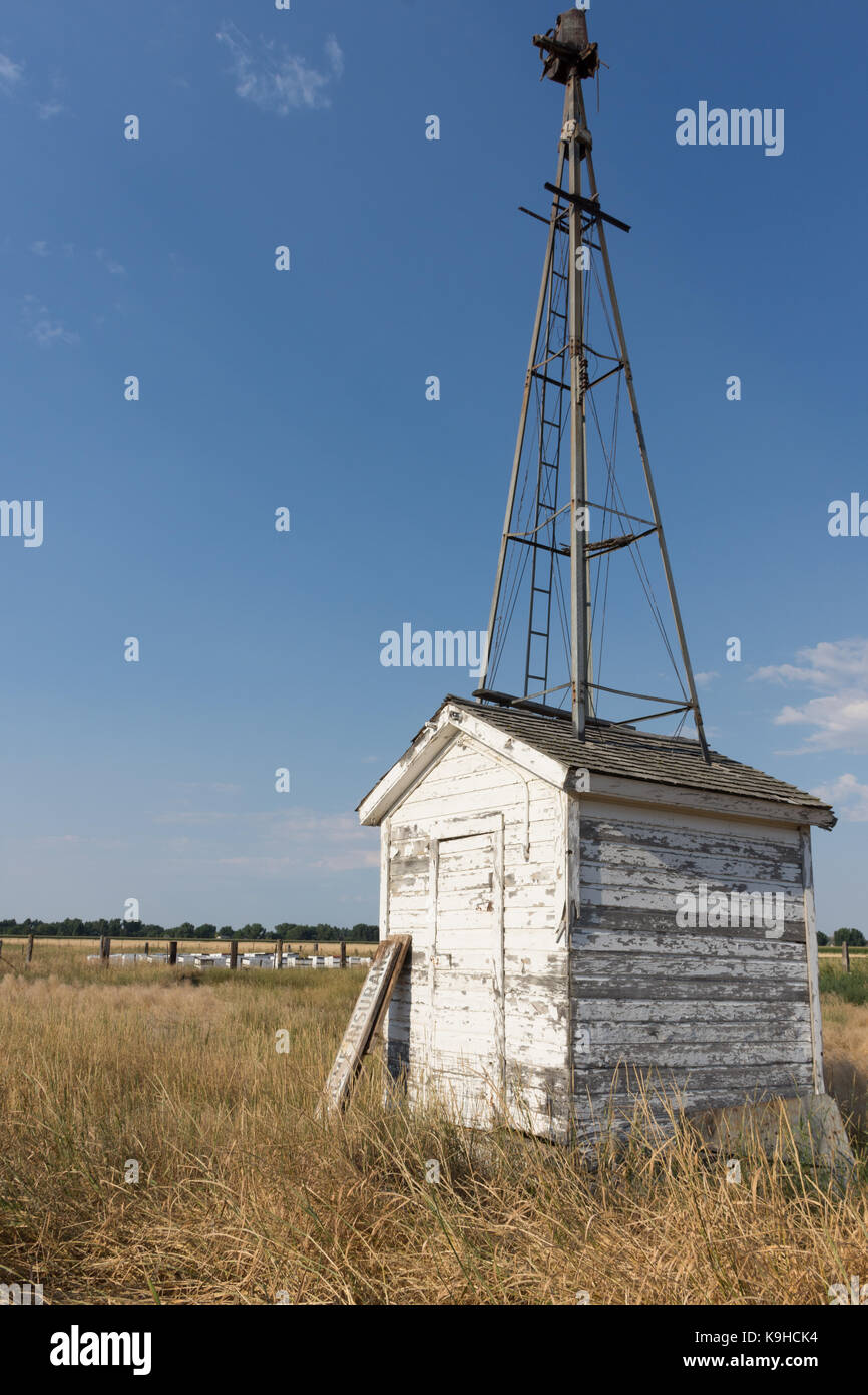 Pump House with weathered siding and the remnants of a windmill on top. Beehives are in the background. Stock Photo