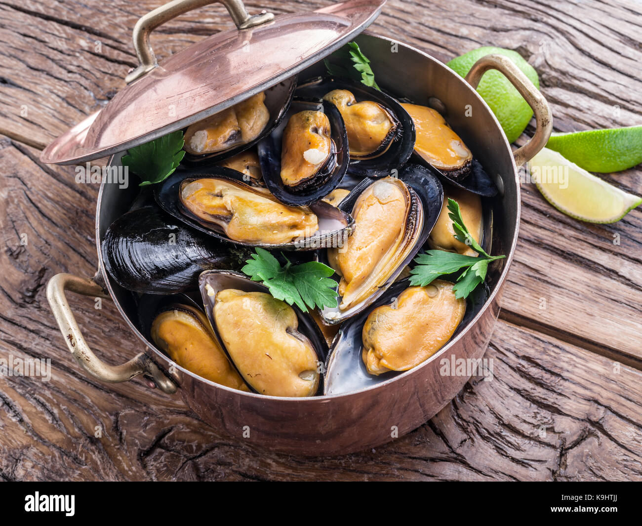 Boiled mussels in copper pan on the wooden table. Stock Photo