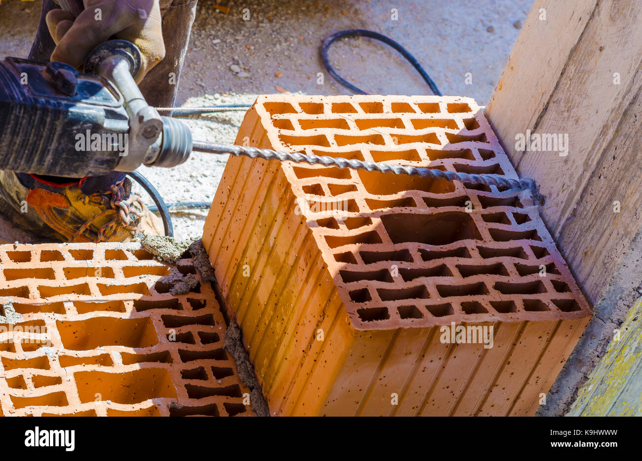 Mason drills a hole with a power drill on a column in of reinforced