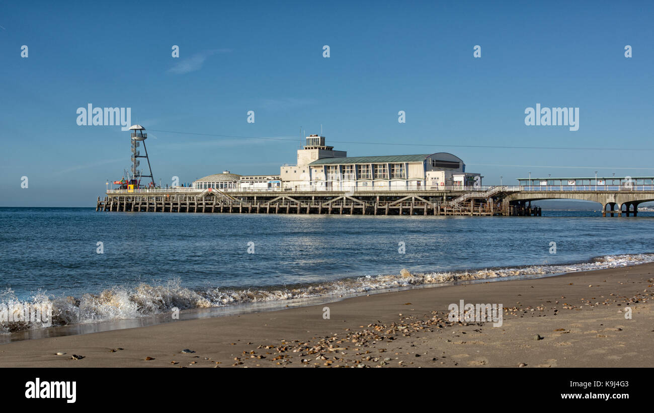 Bournemouth pier from a low angle showing breaking waves on the shore line and a deserted beach Stock Photo