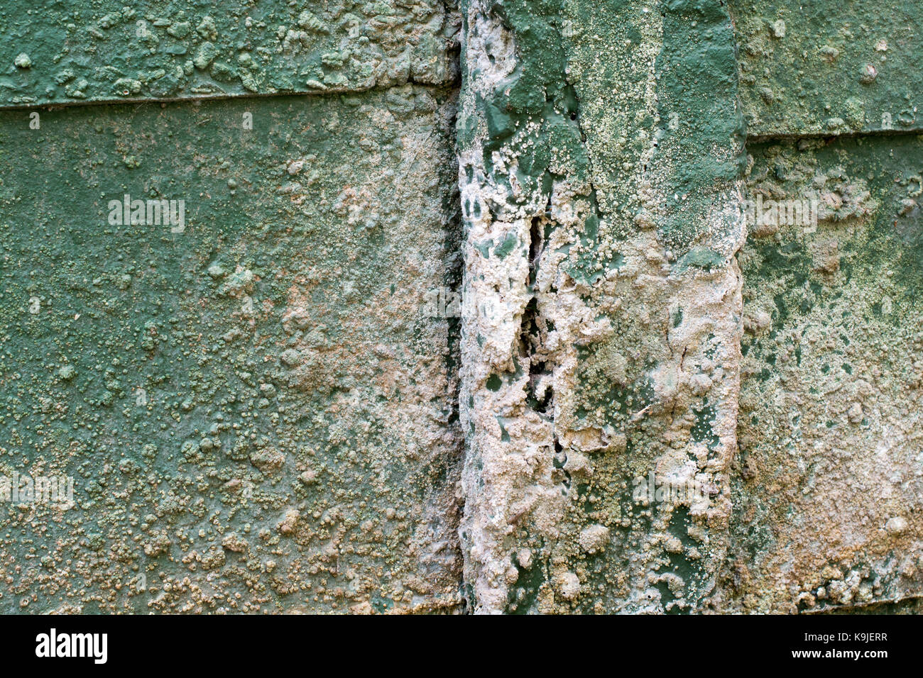Concrete wall pillar in bad condition with crack, bubbling paintwork and signs of efflorescence