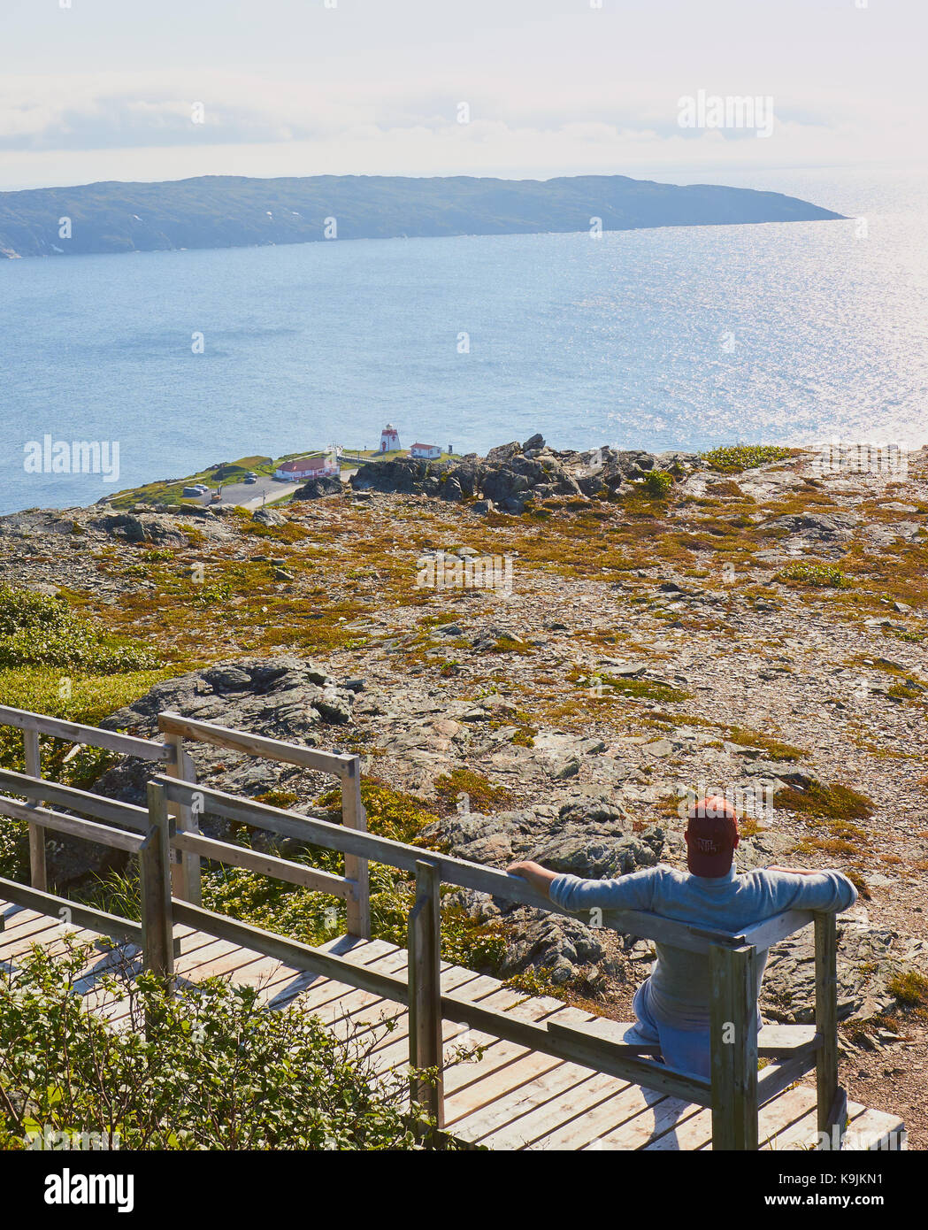 Mid adult male tourist sitting on wooden seat above Fishing Point (Fox Point) Lighthouse, St Anthony, Great Northern Peninsula, Newfoundland, Canada Stock Photo