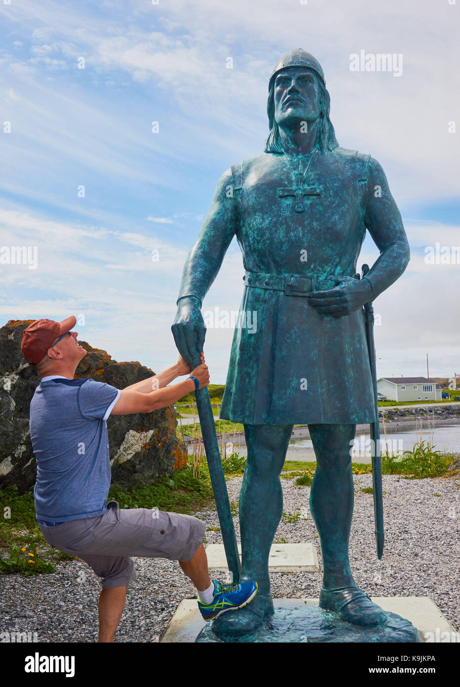 Middle aged male Swedish tourist looking up at 10 foot high bronze statue of Leif Erikson by Phillip Levine,  L'Anse Aux Meadows, Newfoundland, Canada Stock Photo