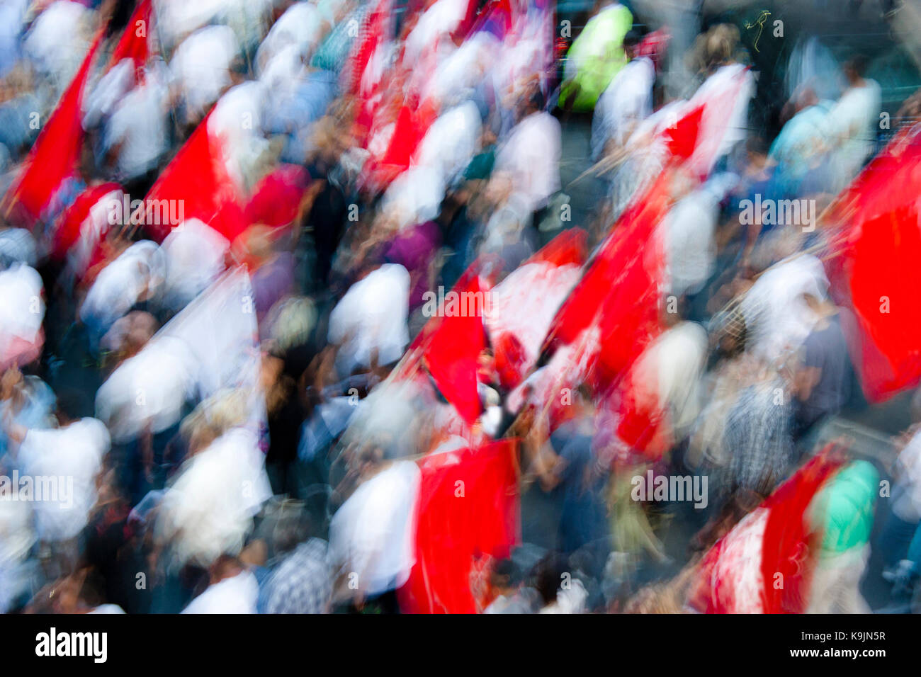 Blurry people in street protest walking with red flags, from above Stock Photo