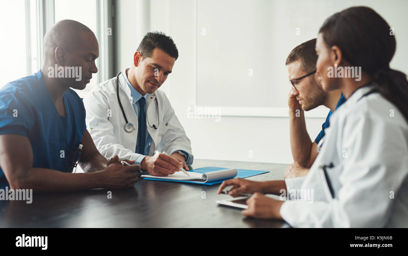 Young medical personal people on staff meeting sitting in front of each other at table in white coats and blue uniform shirts Stock Photo