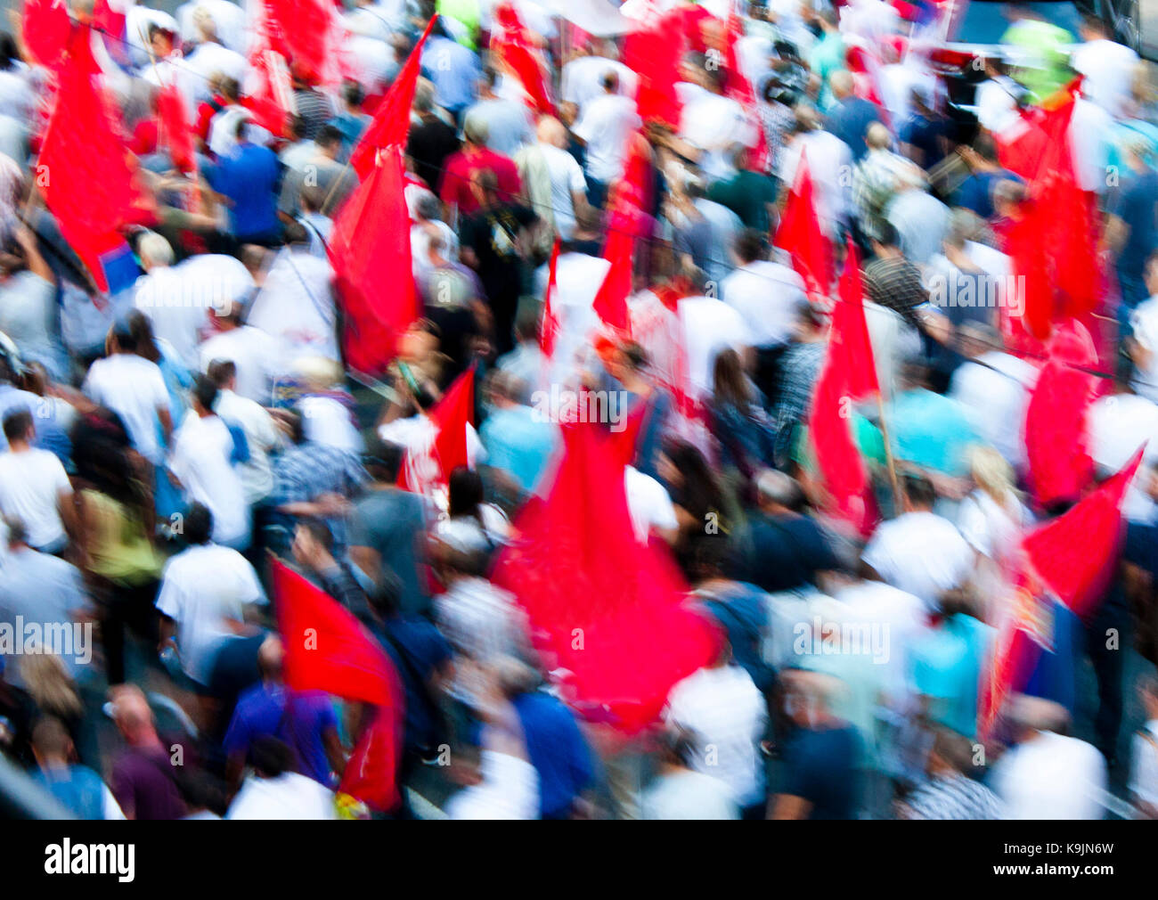 Blurry people in street protest walking with red flags, from above Stock Photo