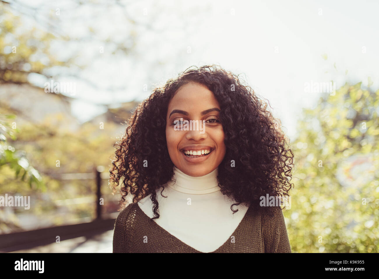 Young woman with curly hair standing outdoors. Smiling woman standing in morning sun. Stock Photo