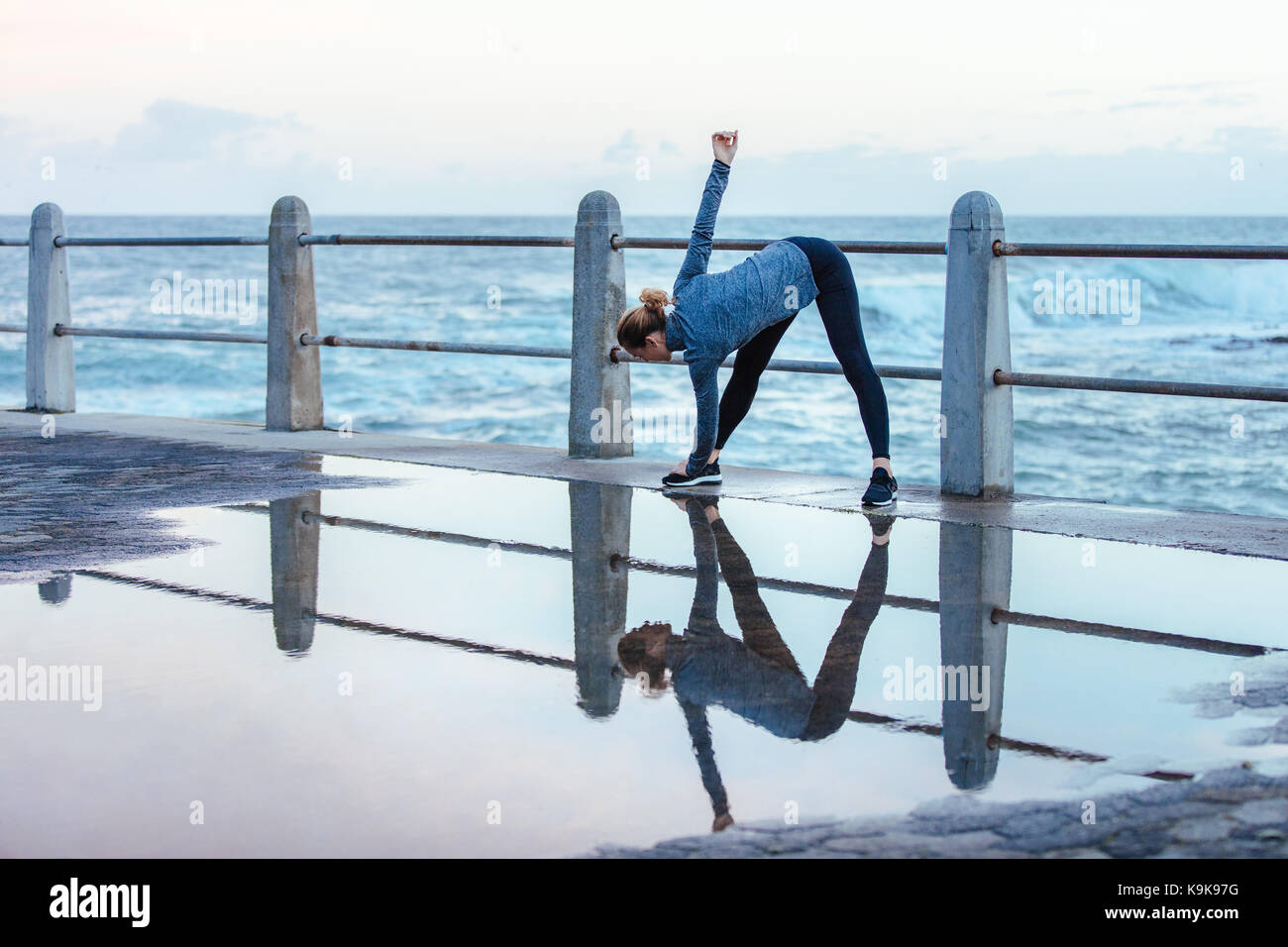 Young woman doing wide legged bend, twisted body exercise along the