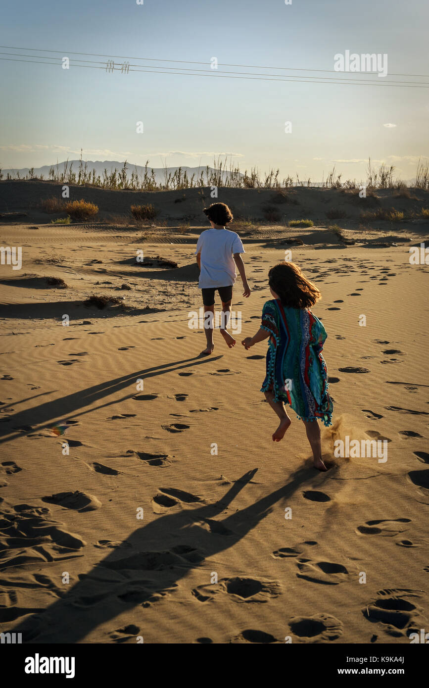 Boy and girl running wild on a sandy beach at sunset leaving footprints Stock Photo