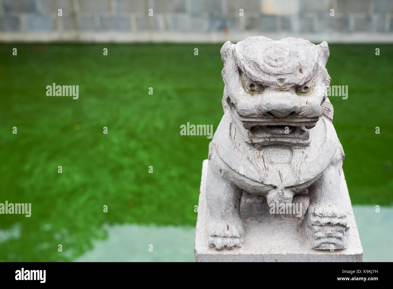 Lion stone statue with a green pond in the background Stock Photo