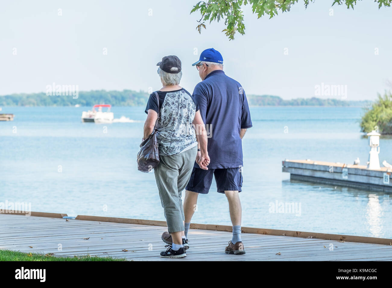 Senior couple walk hand in hand along the boardwalk at the waterfront in Orillia Ontario Canada. Stock Photo