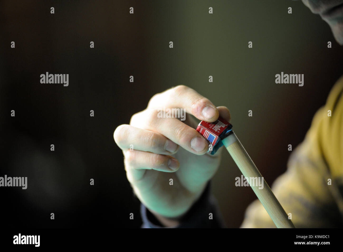 A player's arm rubbing a cue with a cue chalk Stock Photo