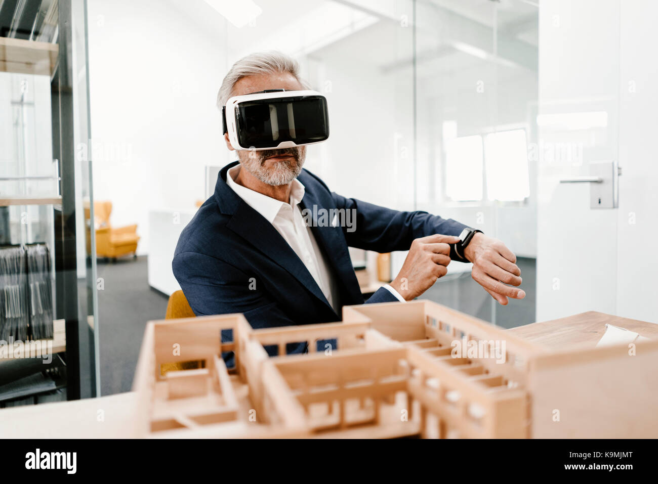 Mature businessman with architectural model in office wearing VR ...