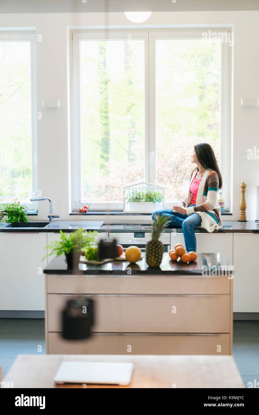 Woman in kitchen looking out of window Stock Photo - Alamy