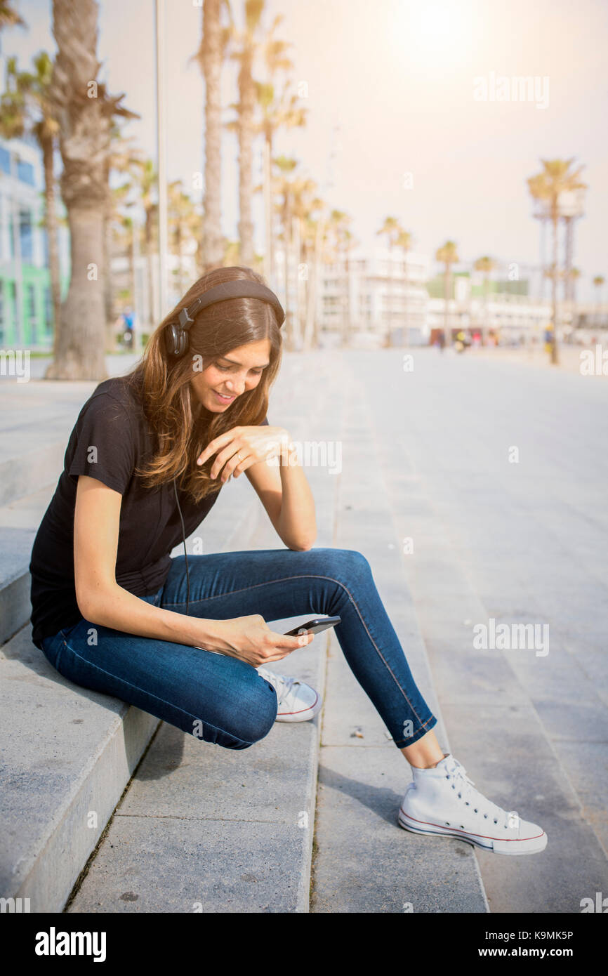 Smiling young woman sitting on steps listening to music Stock Photo - Alamy