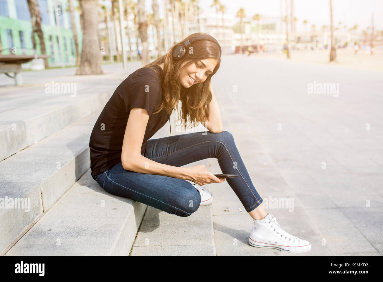Smiling young woman sitting on steps listening to music Stock Photo - Alamy