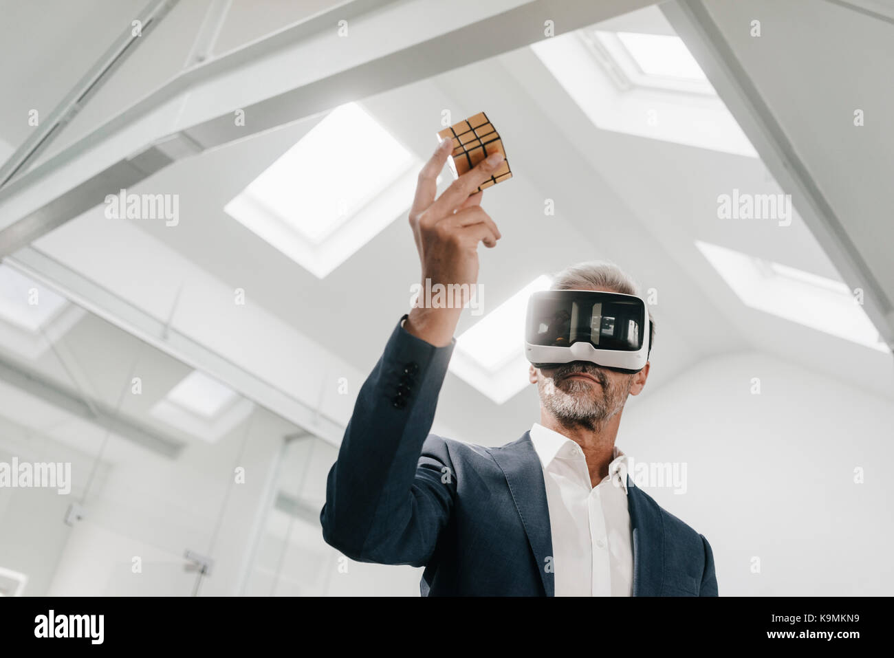 Mature businessman in office wearing VR glasses holding Rubik's Cube ...
