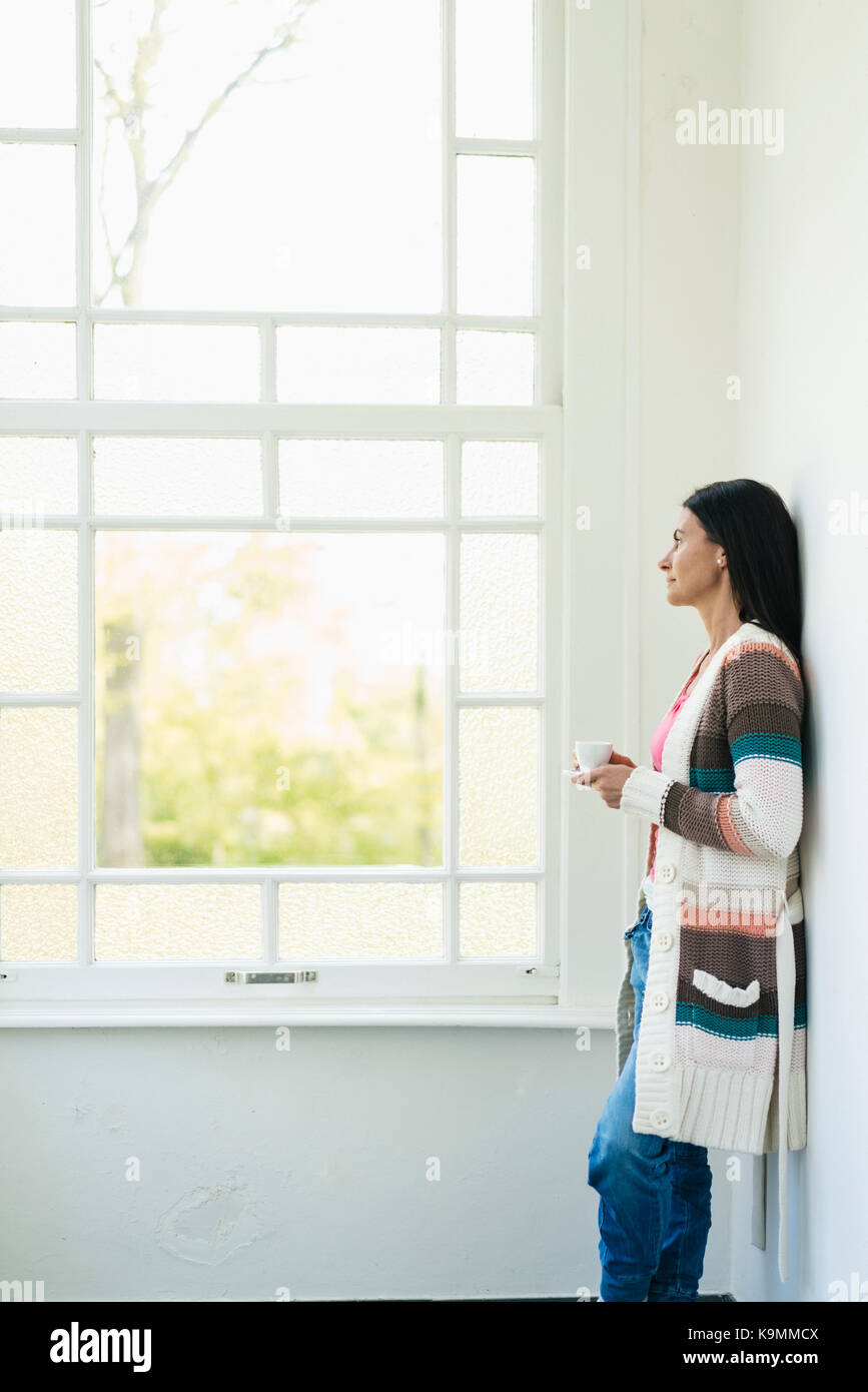 Woman at home looking out of window Stock Photo - Alamy