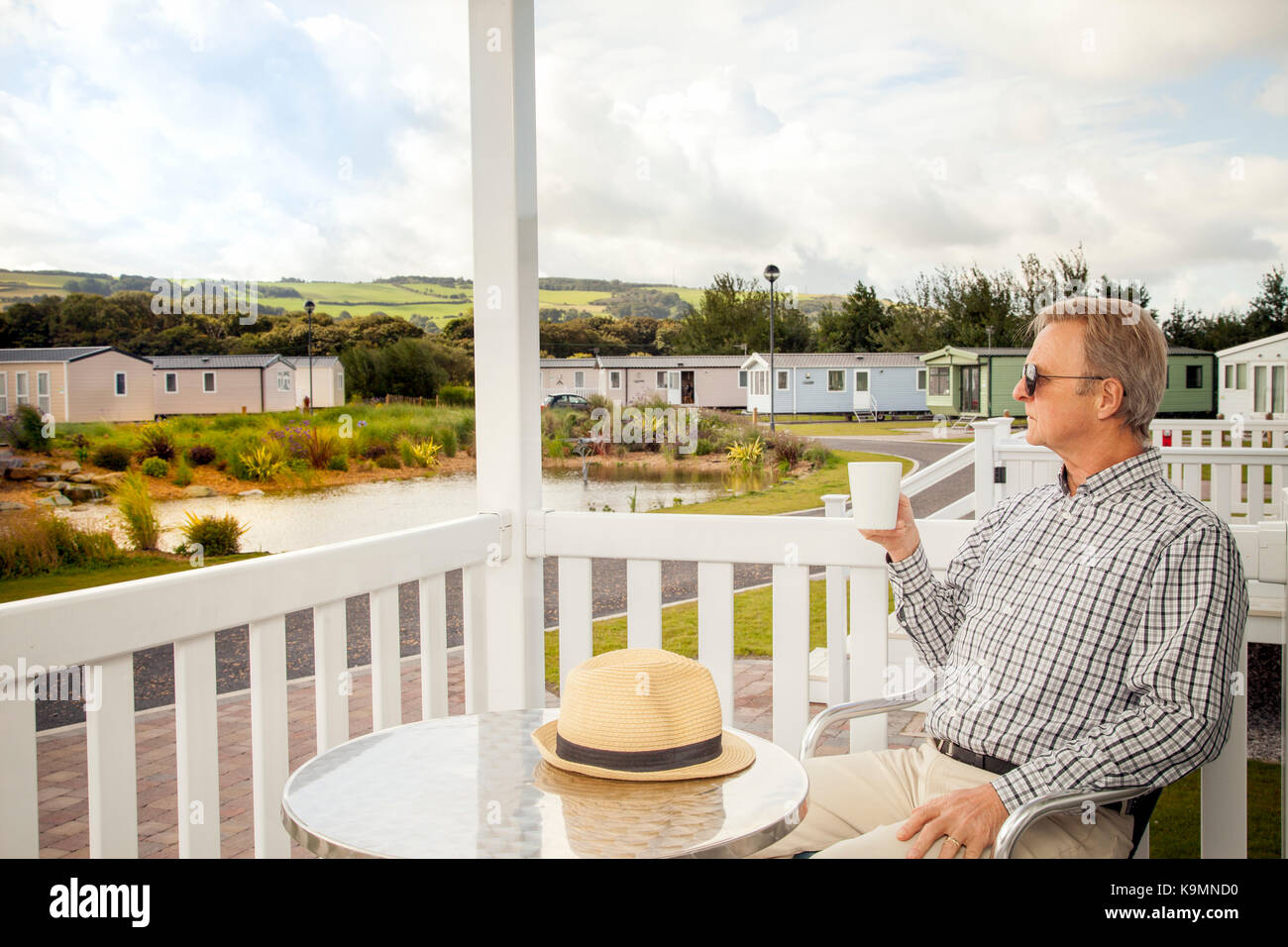 Elderly man drinking a mug of coffee sitting on the veranda of a luxury static caravan in North Wales taking in the scenic views of the Welsh  Country Stock Photo