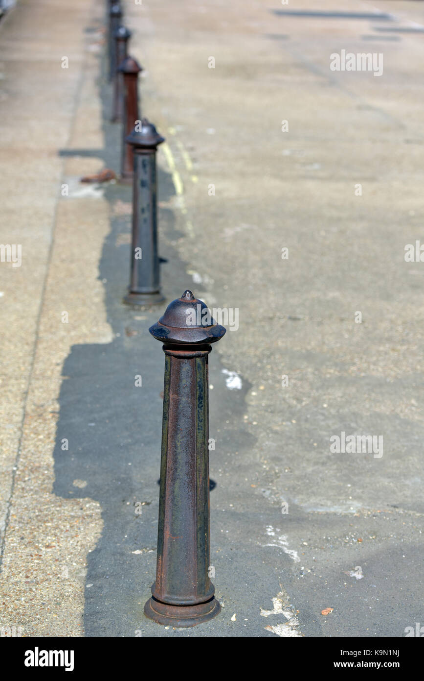 some cast iron bollards in a row on the edge of a pathway, pavement or road. disappearing to a vanishing point. cast iron Victorian architectural. Stock Photo