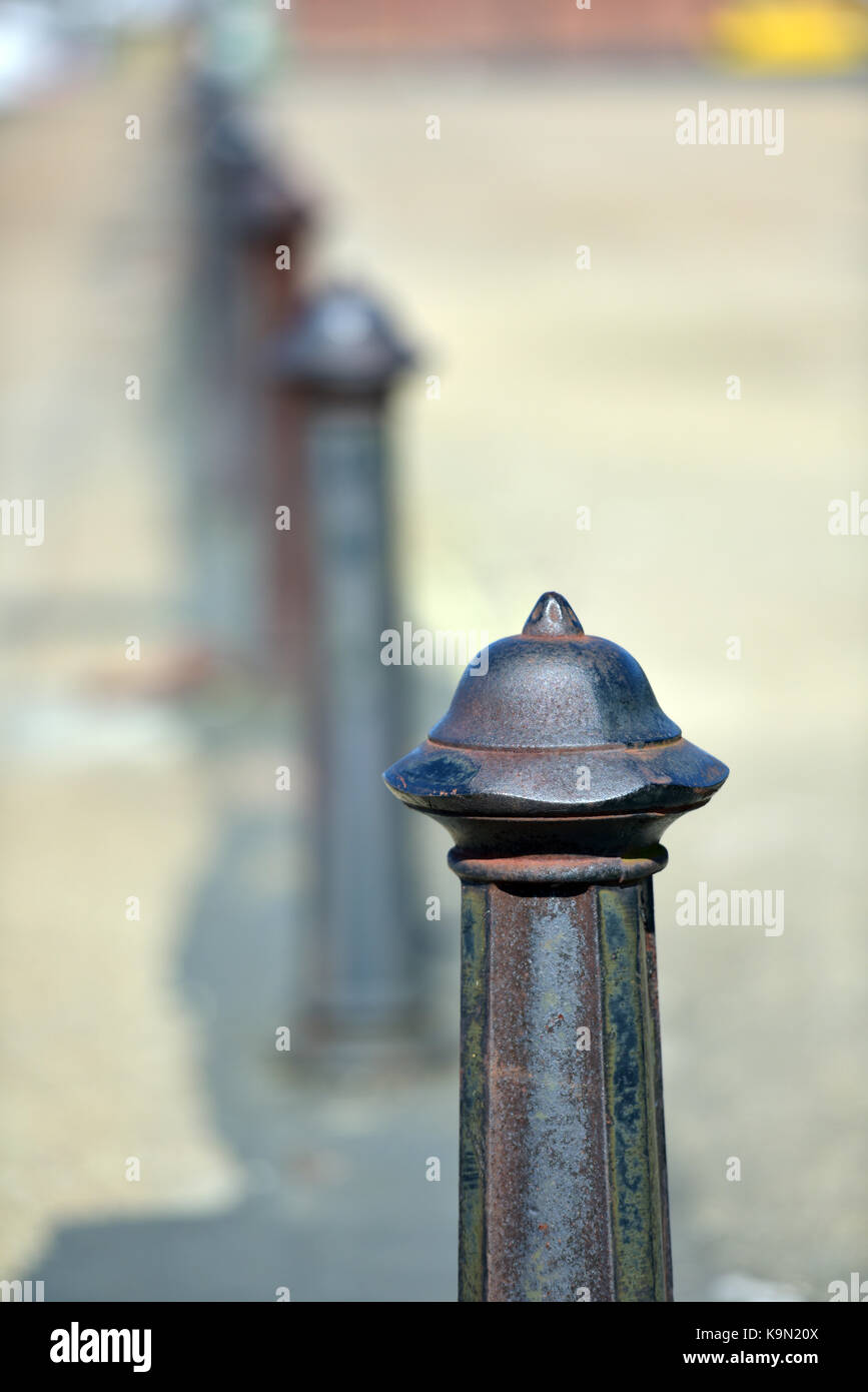 a row or line of cast iron parking bollards to prevent entry into an area going gradually out of focus and disappearing into a blurred background. Stock Photo