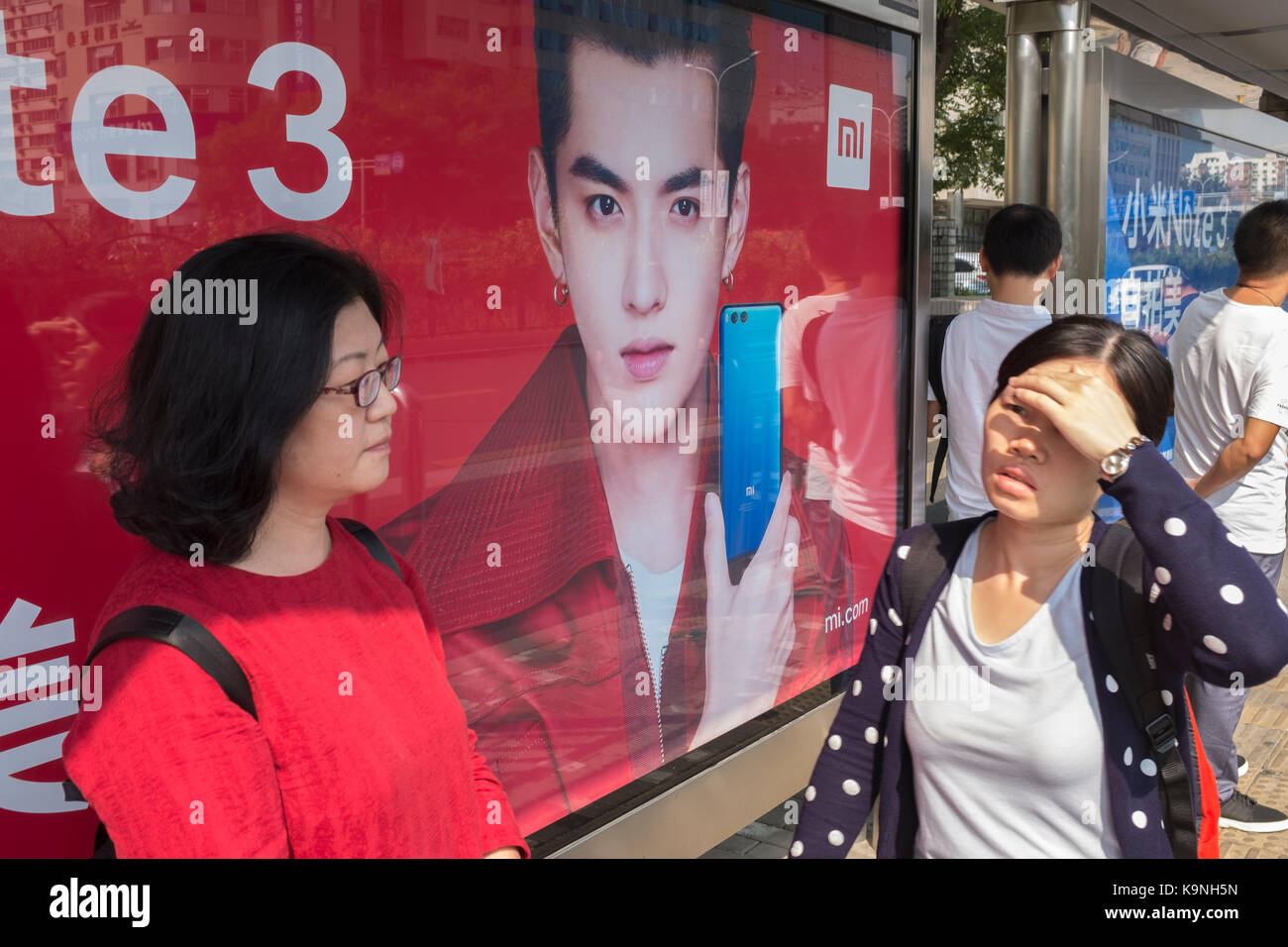 Chinese passenger waiting bus in front of billboard of Kris Wu, Xiaomi's new endorser. Stock Photo