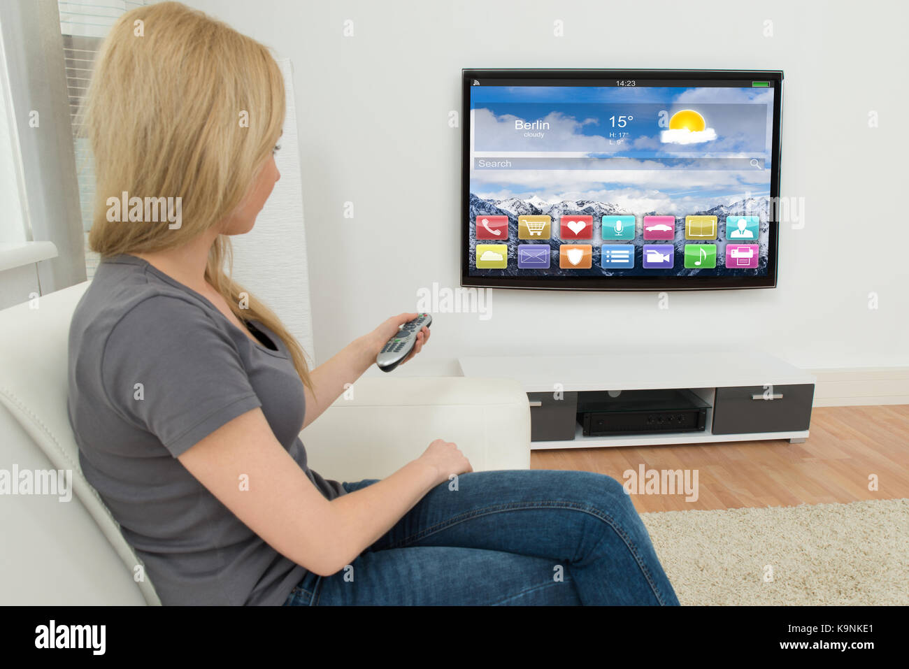 Young Woman On Sofa Holding Remote Control In Front Of Television With Apps Stock Photo