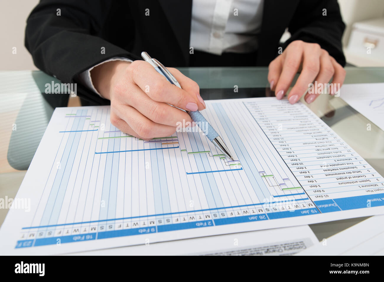 Close-up Of Businesswoman With Pen Working On Gantt Chart At Desk Stock Photo