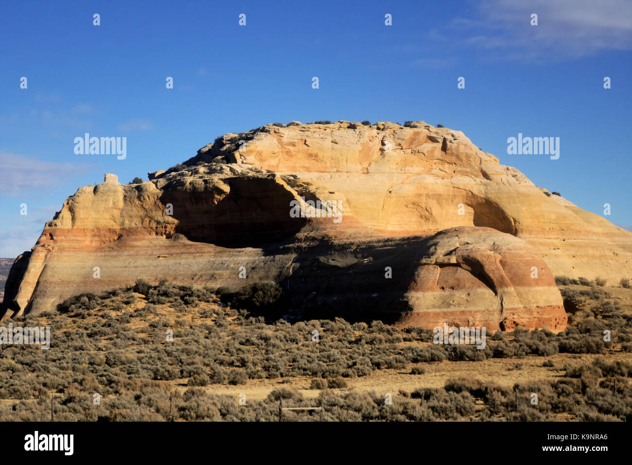 A huge vertical yellow layered sandstone formation on a clear blue sky. Stock Photo