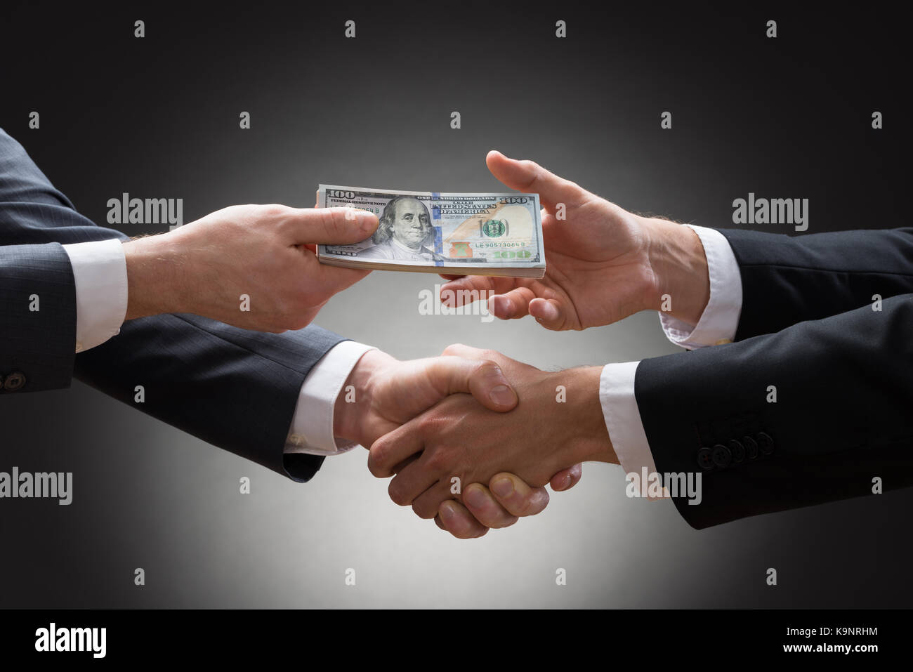 Close-up Of Two Businessmen Shaking Hands And Receiving Banknote Stock Photo
