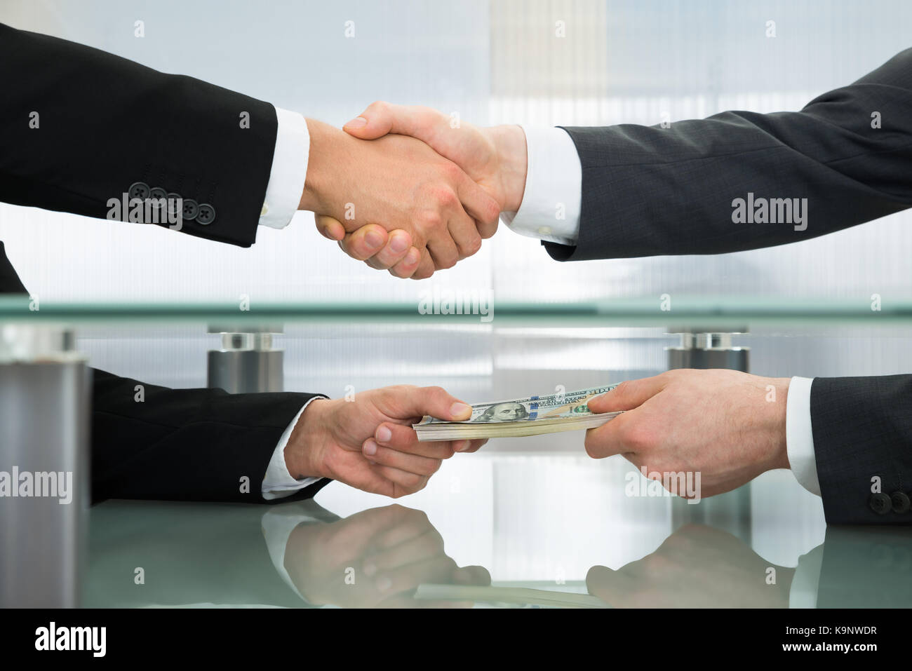 Close-up Of Businessman With Money Handshaking With His Business Partner Stock Photo