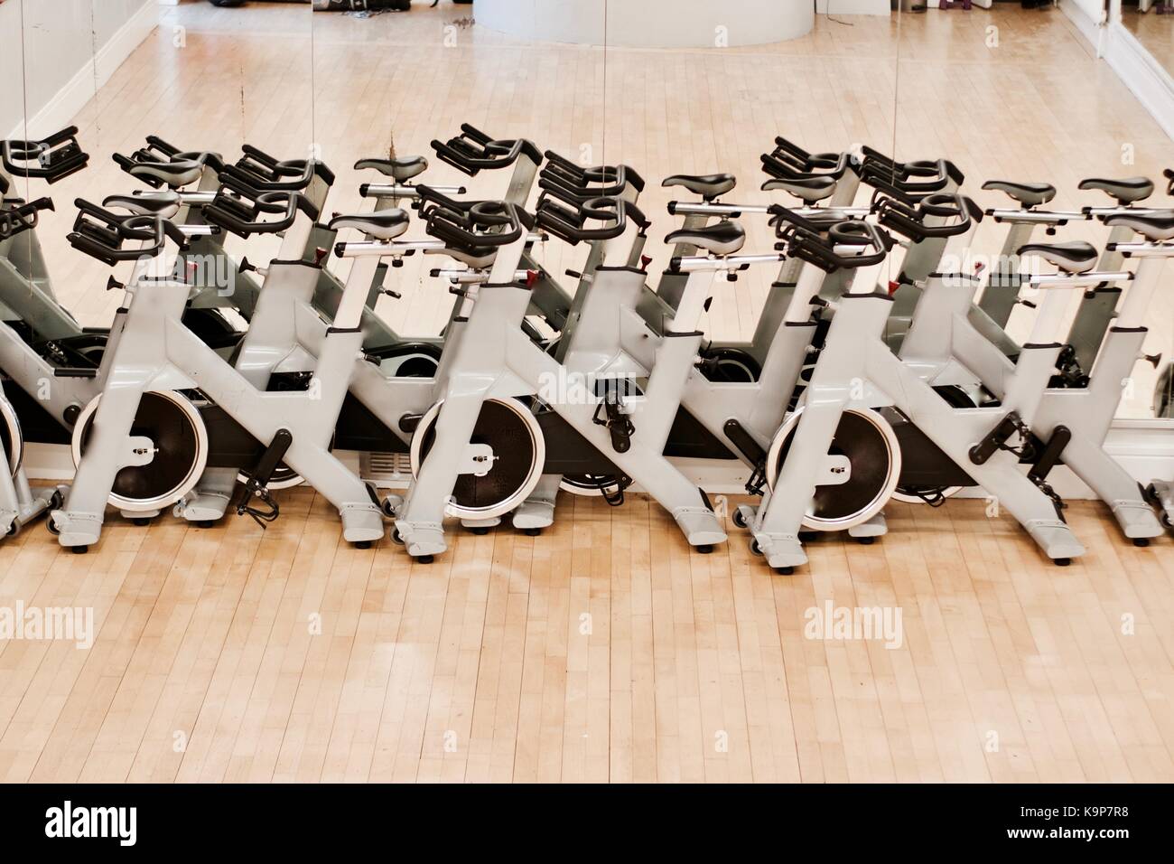 Grey exercise bicycles on the gym staying near mirror on the wooden floor. Stock Photo