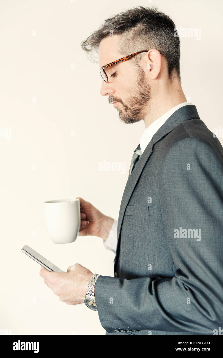 Side profile view portrait of professional businessman holding mobile phone and coffee mug wearing eye glasses. Stock Photo